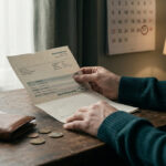 Un homme examine un relevé bancaire avec un solde négatif devant un calendrier et un portefeuille sur un bureau.